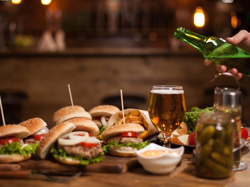 Man hand pours larger beer in a glass standing on a vintage table .Blurred counter bar . Jar of pickles.